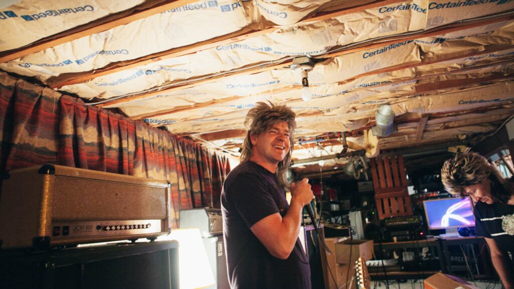 Man with mullet holding microphone in basement